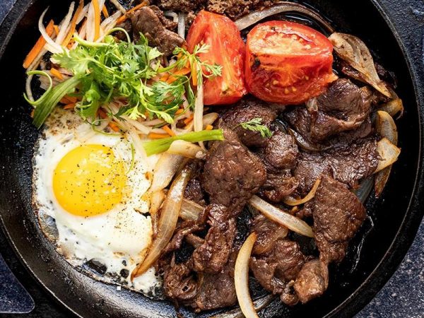 Vietnamese bo ne with beef steak and sunny-side-up fried egg on a sizzling hot plate