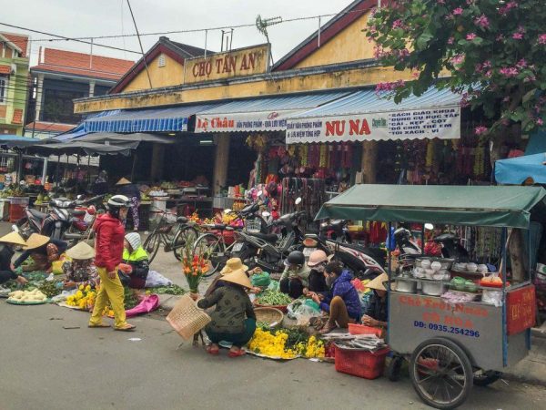 Local residents shopping at Tan An Market in Hoi An, Vietnam, surrounded by fresh produce stalls.